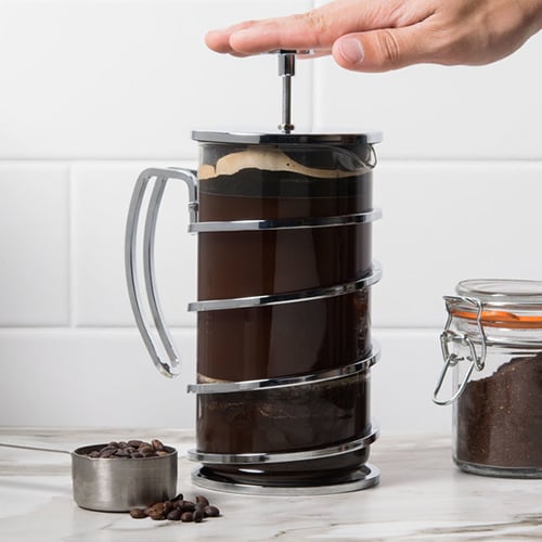 A hand pushing the handle of a french press coffee maker down
