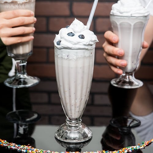 Blueberry milkshake in a milkshake glass with a straw