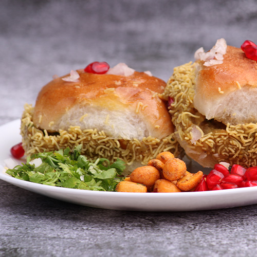 Indian Dabeli snack served with Pomegranate Seeds and Cilantro in white ceramic plate