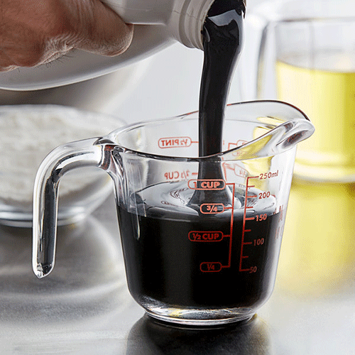 close up of black strap molasses being poured into a measuring cup