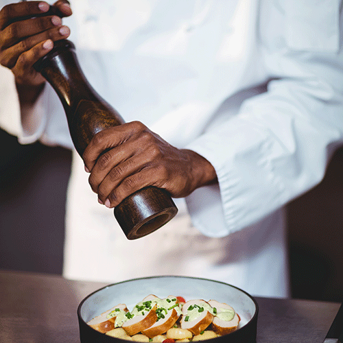 mid section of chef sprinkling pepper on a salad