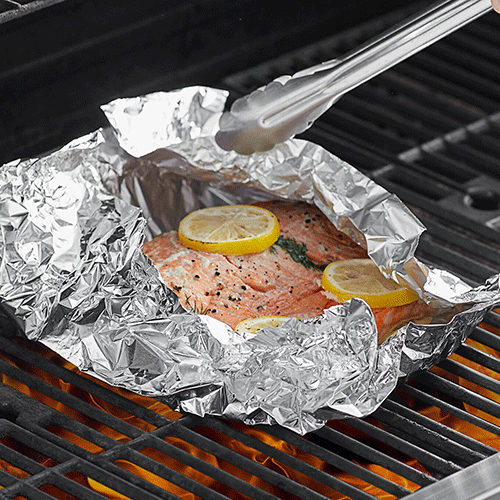 salmon in foil cooking on grill with lemon