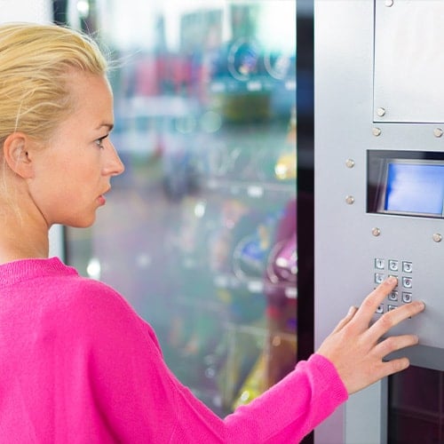 woman in a bright pink shirt purchasing food at a vending machine