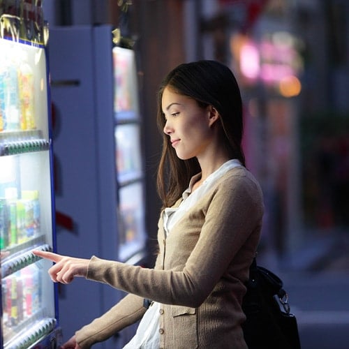 woman selecting an item from a vending machine in the street at night