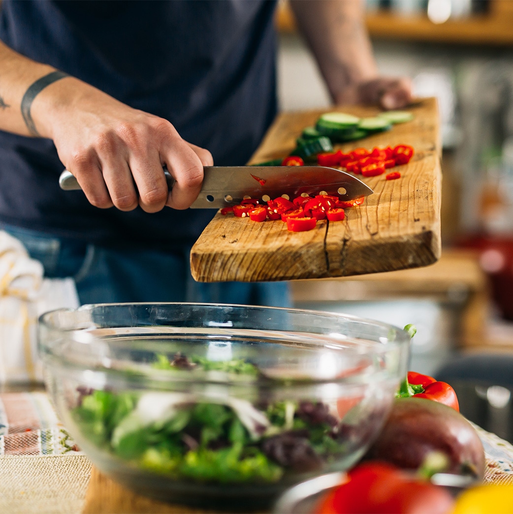 chef adding chopped up peppers to a bowl of ingredients