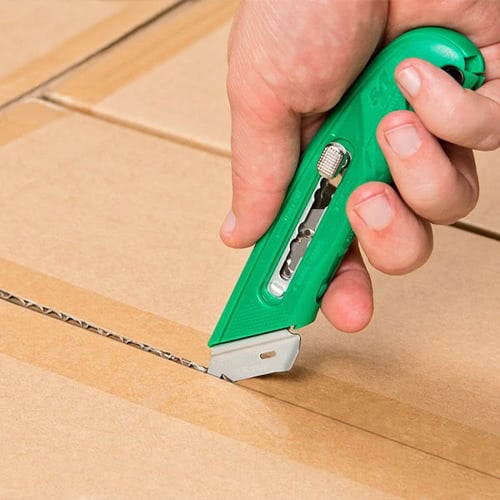 person’s hand using green box cutter on cardboard box