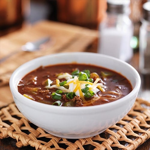 bowl of chili with sour cream and cheese in a white bowl