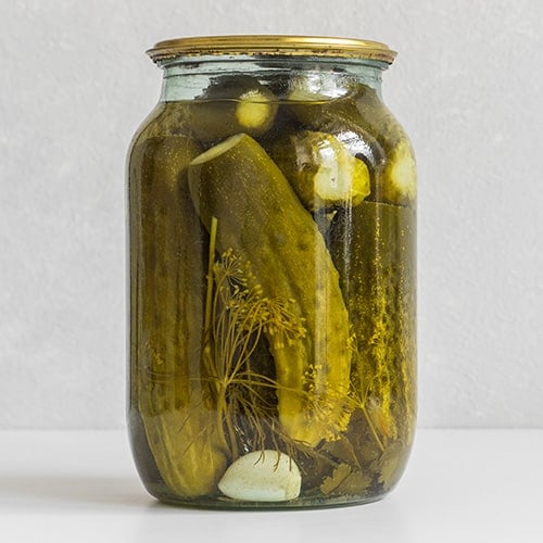 glass jar with homemade full sour pickles on a white background