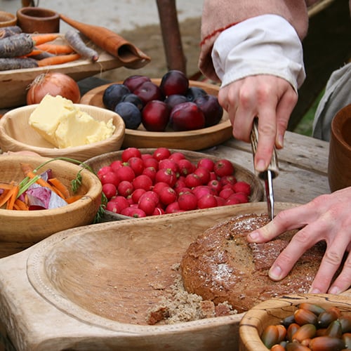 hobbit hands cutting bread with a knife on a table of assorted foraged foods