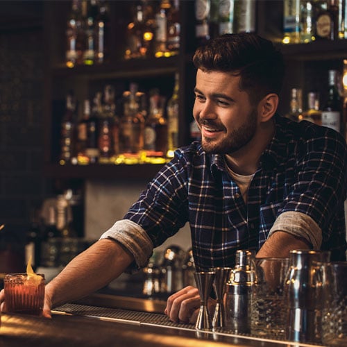 A bartender smiles while pushing a customer's drink order forward