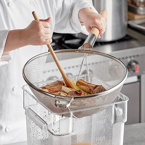 soup stock being filtered through a large strainer into a container