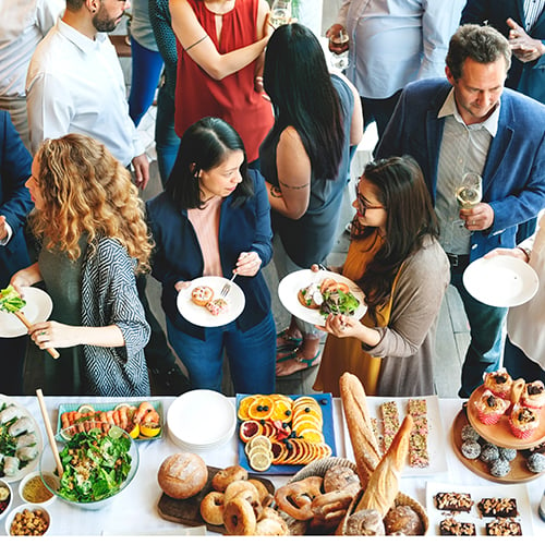 Crowd of people gathered around a buffet table with assorted foods