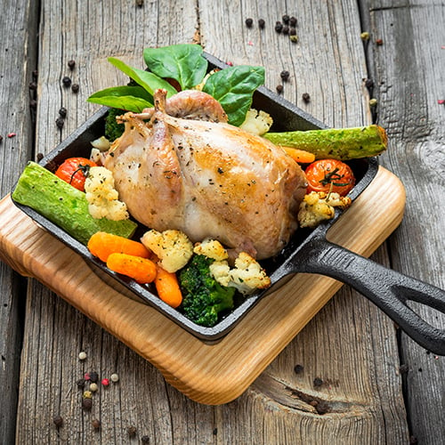 grilled pheasant in a cast iron served over colorful vegetables