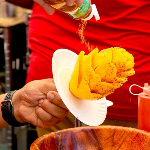 seasoning a sliced mango on a stick with tajin