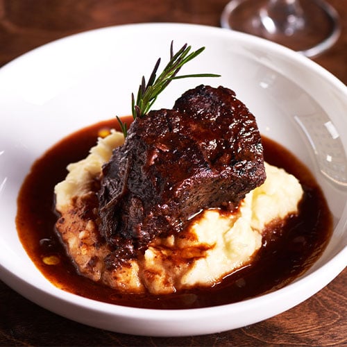 Short ribs served over mashed potatoes in a demi glace sauce topped with a rosemary sprig.