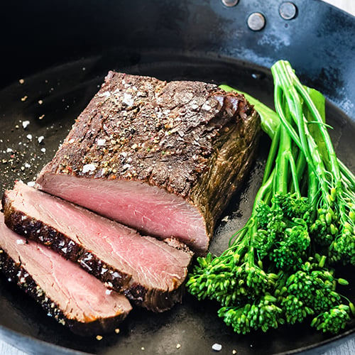 sliced ostrich in a black pan served with broccolini and a sea salt finish