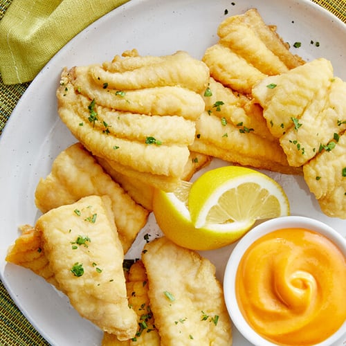 Fried fish with remoulade sauce and lemon wedges on a white plate