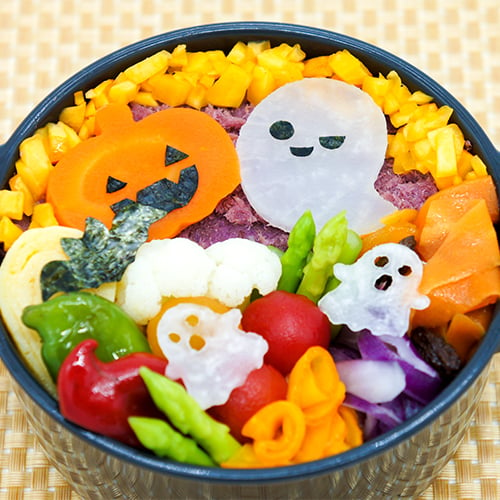 A Halloween themed decorated bento box featuring veggies cut to look like ghosts and pumpkins