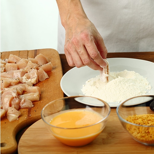 A chef dredges boneless wings in an egg wash and flour.
