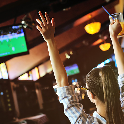 Woman with a beer watching sports on a bar television