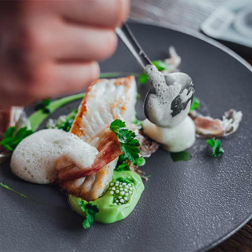 close up of a hand finishing plating for an elegant seafood dish
