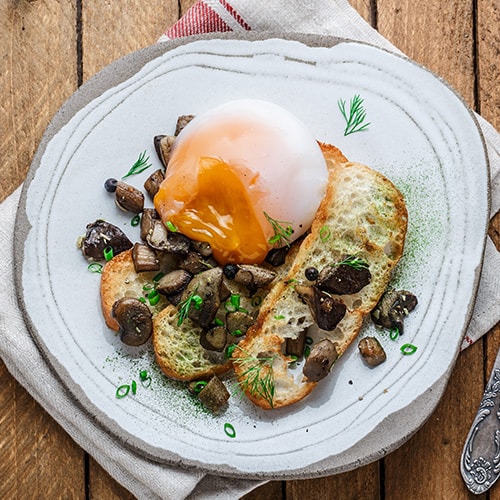 close view of a poached egg with wild mushrooms and toasted bread