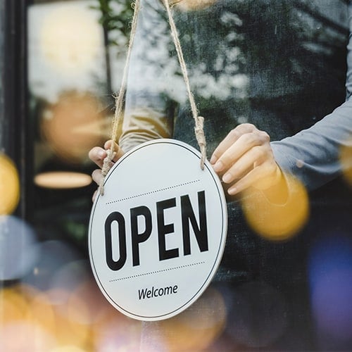 employee-turning an open sign hung in a business window