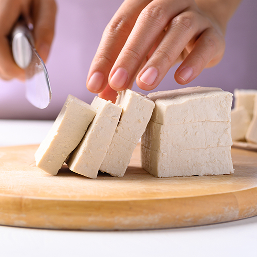 Hands slicing tofu with a knife