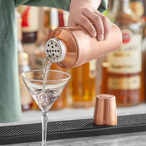 bartender using a shaker to pour a drink into a martini glass