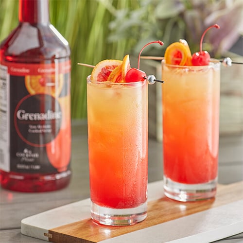 Grenadine syrup next to two brightly colored cocktails