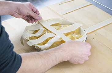 Take the two strips of dough on either side of the center strip and gently lift them, folding them back halfway. Place another strip of dough horizontally across the pie filling, above the folded strip. Unfold the folded strip back over the horizontal strip. Repeat this process with the remaining vertical strips, alternating over and under each horizontal strip.