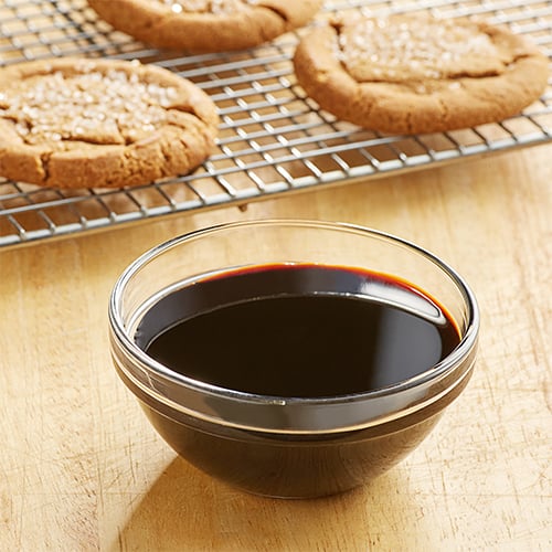 small bowl of molasses in front of molasses cookies on a cooling rack