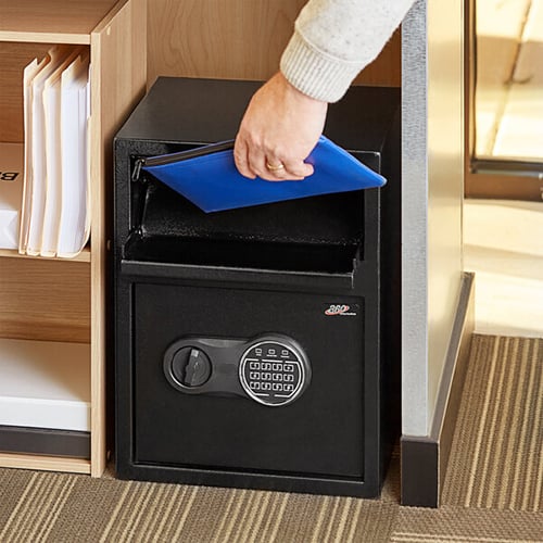 hand placing blue folder into black floor safe