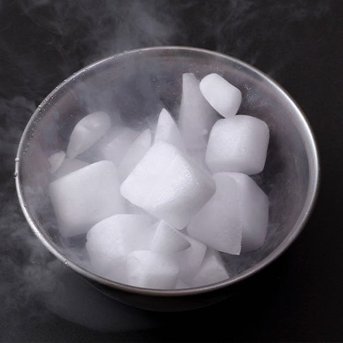 Tray of dry ice chunks creating fog effect on a dark table