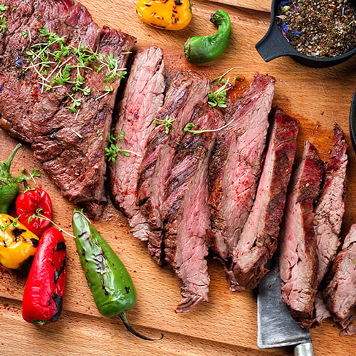 Grilled flat iron steak on a wooden cutting board with grilled peppers