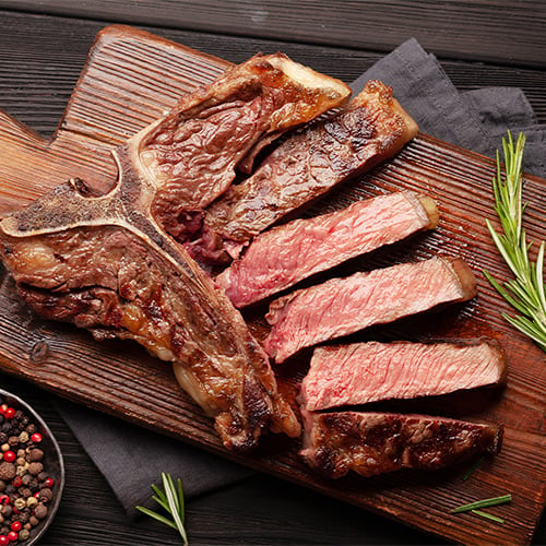 T-bone grilled beef steak on wooden board with rosemary and peppercorns
