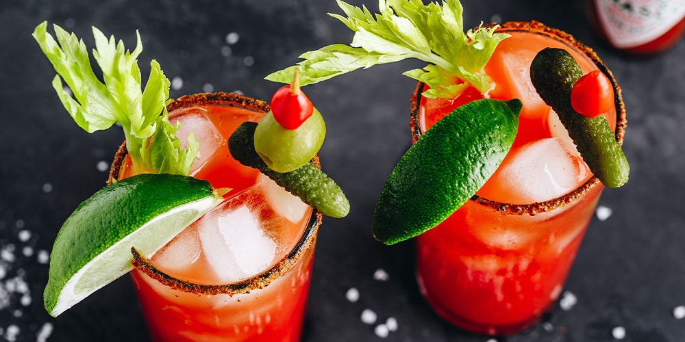 Top view of two Bloody Marys with pickle lime olive and celery garnishes