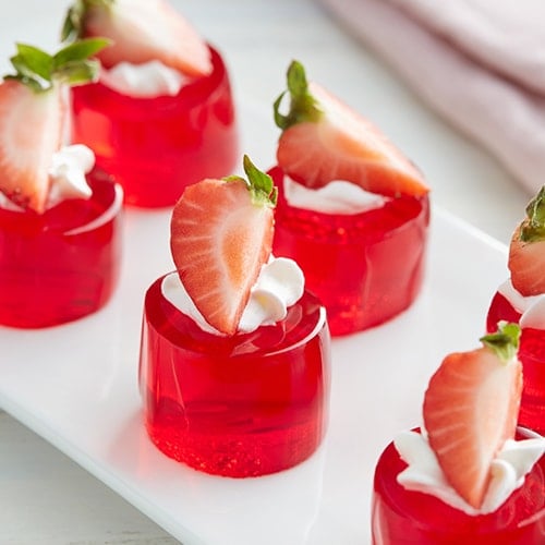 Red jelly desserts topped with whipped cream and strawberries