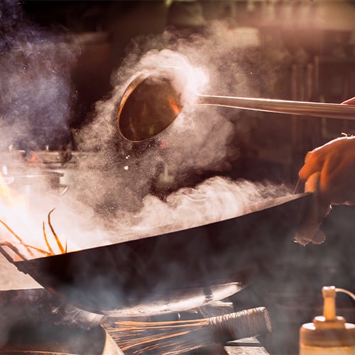 Extreme smoke surrounding a wok over a flame on a stove