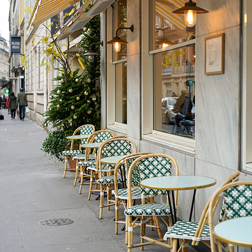 empty, green and white patterned chairs and tables on a sidewalk outside of a cafe