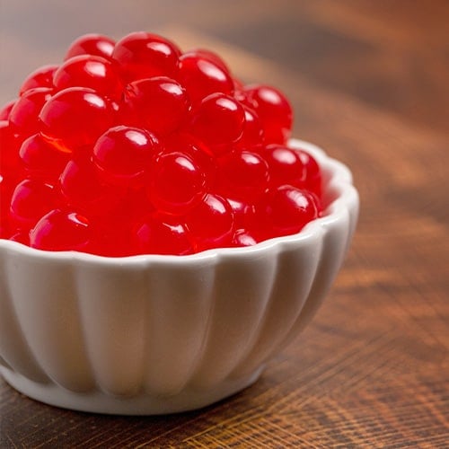 red popping boba in a white bowl on a wood table