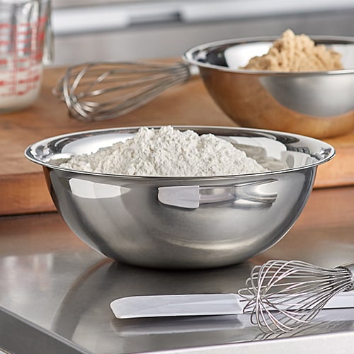 Mixing bowl filled with flour with whisk and spatula in foreground