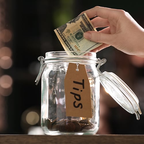 Hand putting twenty dollar bill into tip jar
