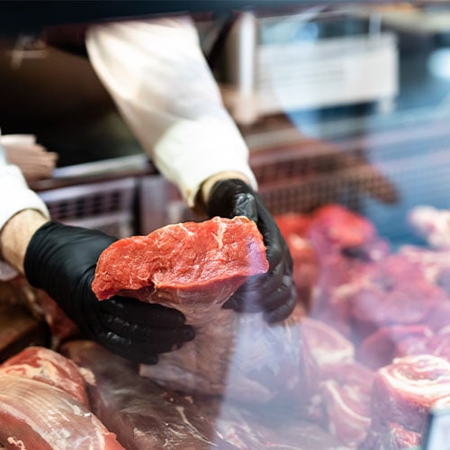 butcher holding up piece of beef in display case
