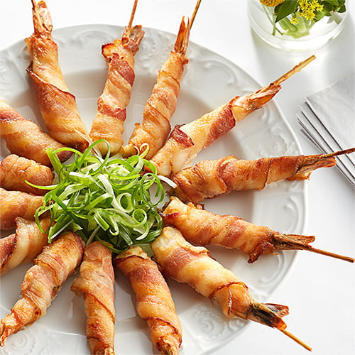 Smoked bacon wrapped around shrimp skewers on a plate