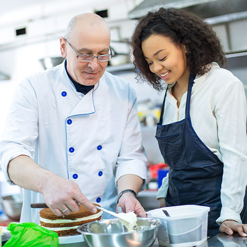 Older chef teaching younger chef