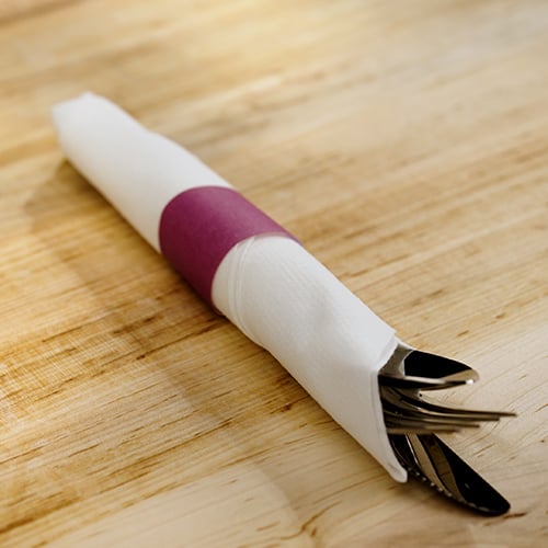 silverware rolled into a white paper napkin with red napkin wrap