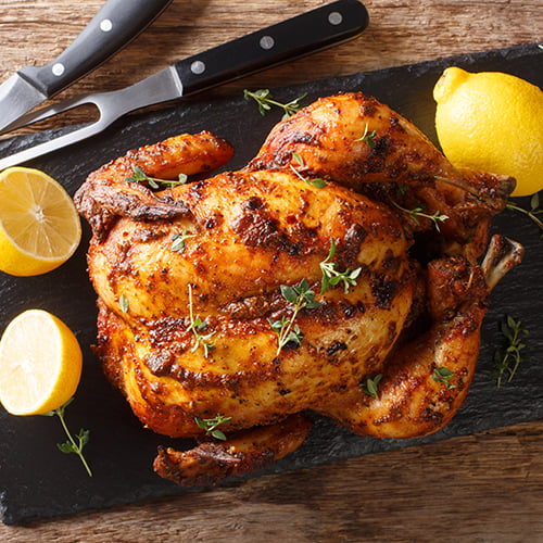 a rotisserie whole chicken with lemons and carving utensils