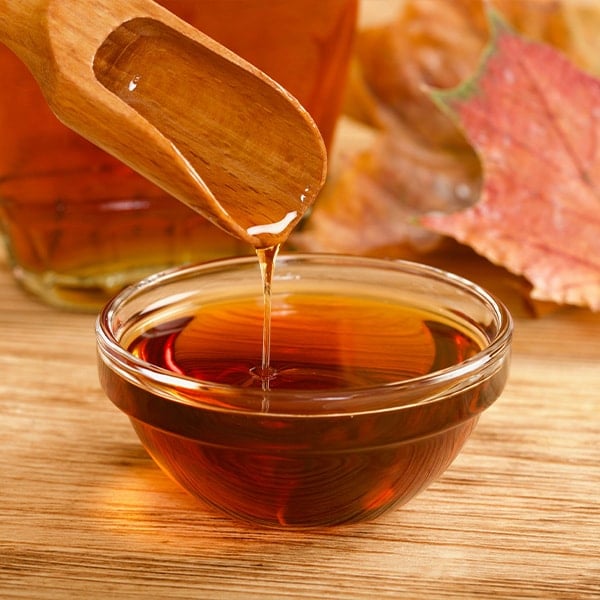 wooden spoon and dish of maple syrup with leaves in the background