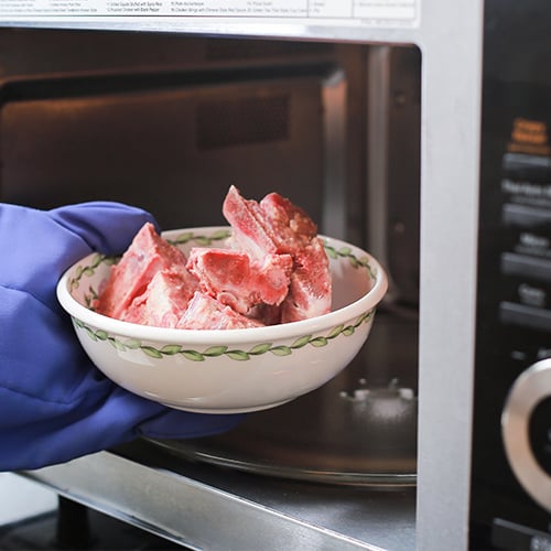 bowl of frozen meat being put in microwave to defrost
